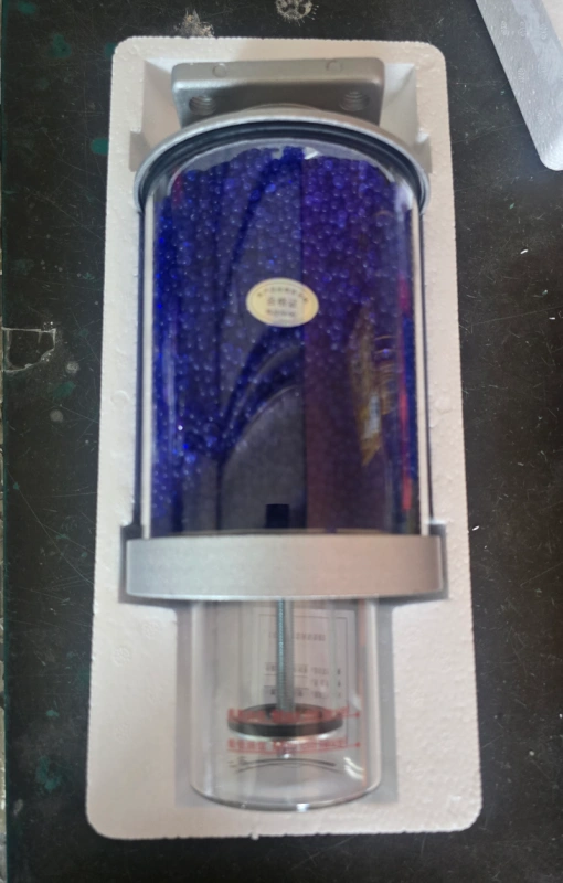 Clear tube silica gel breather with blue indicating desiccant inside, equipped with metal fittings and oil trap, applied on oil transformers to remove moisture and dust from incoming air.